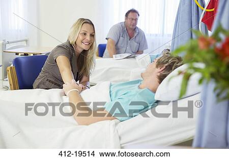 Woman holding boyfriend's hand in hospital room View Large Photo Image Picture - Woman holding boyfriend's hand in hospital room. Fotosearch