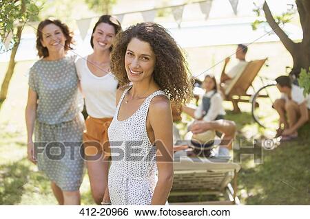 Stock Photograph - Woman smiling outdoors with family near. Fotosearch
