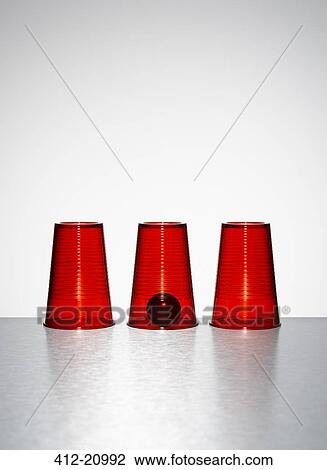 Stock Image - Ball under middle of three clear red cups. Fotosearch