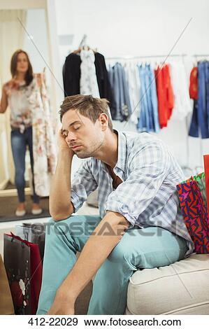 Bored man shopping with girlfriend in clothing store View Large Photo Image Stock Photo - Bored man shopping with girlfriend in clothing store. Fotosearch