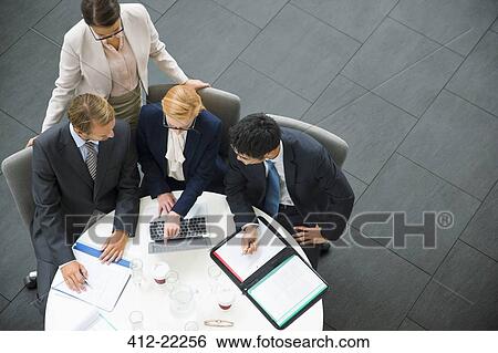 Stock Photograph - Business people gathered around laptop in office building. Fotosearch