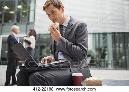 Stock Photo - Businessman eating lunch while working outside office building. Fotosearch