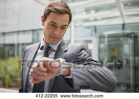 Businessman looking at watch outside office building View Large Photo Image Stock Photography - Businessman looking at watch outside office building. Fotosearch