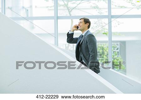 Businessman talking on cell phone on stairs of office building View Large Photo Image Stock Photo - Businessman talking on cell phone on stairs of office building. Fotosearch