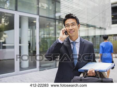 Stock Image - Businessman talking on cell phone outside of office building. Fotosearch