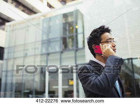 Stock Photograph - Businessman talking on cell phone outside of office building. Fotosearch