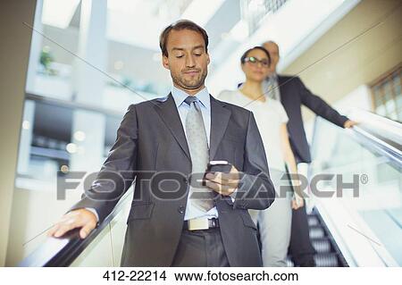 Picture - Businessman using cell phone on escalator in office building. Fotosearch