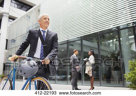 Businessman walking bicycle outside of office building View Large Photo Image Stock Image - Businessman walking bicycle outside of office building. Fotosearch