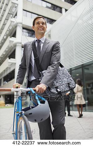 Businessman walking bicycle outside of office building View Large Photo Image Stock Photo - Businessman walking bicycle outside of office building. Fotosearch
