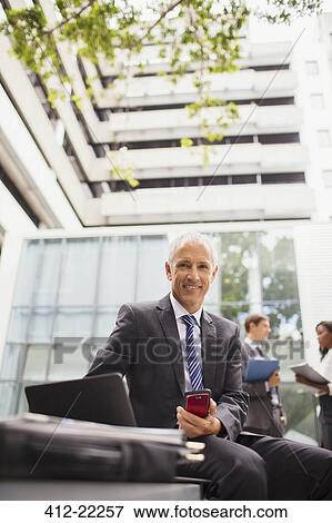 Businessman working on bench outside of office building View Large Photo Image Stock Photo - Businessman working on bench outside of office building. Fotosearch