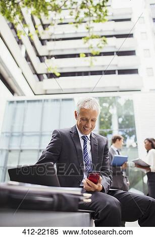 Stock Photography - Businessman working on bench outside of office building. Fotosearch