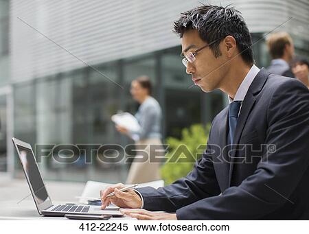Stock Photography - Businessman working on laptop outside of office building. Fotosearch