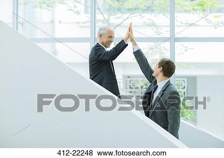 Businessmen high fiving on staircase of office building View Large Photo Image Stock Photo - Businessmen high fiving on staircase of office building. Fotosearch
