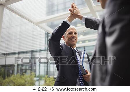 Stock Photograph - Businessmen high fiving outside of office building. Fotosearch