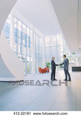 Stock Image - Businessmen shaking hands in office building. Fotosearch