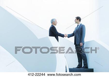 Picture - Businessmen shaking hands on staircase of office building. Fotosearch