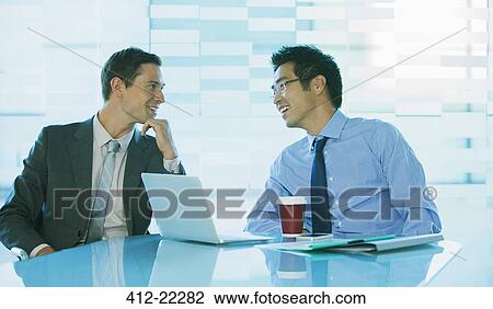 Businessmen talking at table in office building View Large Photo Image Stock Image - Businessmen talking at table in office building. Fotosearch