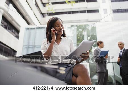 Picture - Businesswoman talking on cell phone looking at documents . Fotosearch