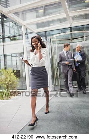 Businesswoman talking on cell phone walking out of office building View Large Photo Image Stock Image - Businesswoman talking on cell phone walking out of office building. Fotosearch