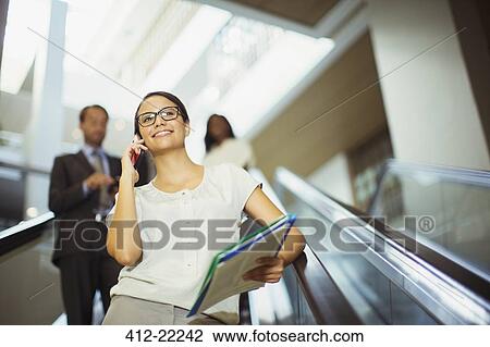 Businesswoman talking on cell phone while going down escalator View Large Photo Image Stock Image - Businesswoman talking on cell phone while going down escalator. Fotosearch