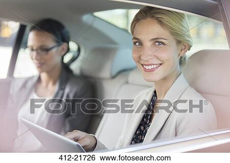 Stock Photograph - Businesswoman using digital tablet in car back seat. Fotosearch