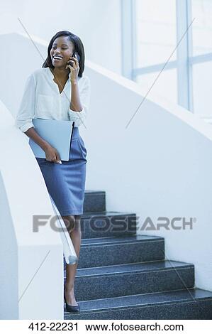 Stock Image - Businesswoman walking on cell phone on stairs of office building. Fotosearch