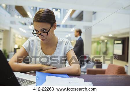 Stock Image - Businesswoman working on laptop in office building. Fotosearch