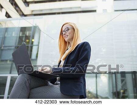 Businesswoman working on laptop outside office building View Large Photo Image Stock Image - Businesswoman working on laptop outside office building. Fotosearch