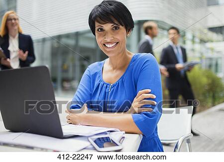 Stock Photo - Businesswoman working on laptop outside of office building. Fotosearch