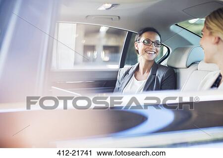 Stock Image - Businesswomen talking in car back seat. Fotosearch