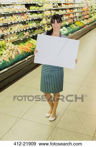 Clerk holding blank card in produce section of grocery store View Large Photo Image Stock Photo - Clerk holding blank card in produce section of grocery store. Fotosearch
