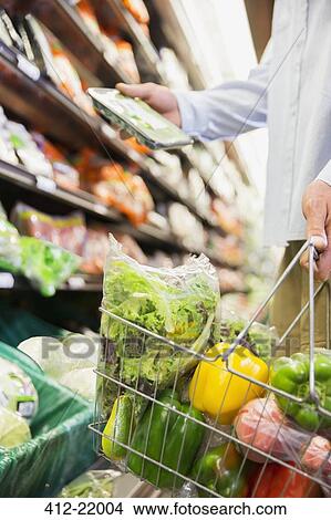 Close up of man holding full shopping basket in grocery store View Large Photo Image Picture - Close up of man holding full shopping basket in grocery store. Fotosearch