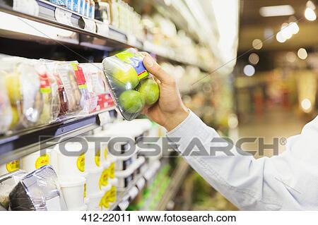 Stock Image - Close up of man holding produce in grocery store. Fotosearch