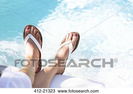 Stock Image - Close up of woman's feet dangling over swimming pool. Fotosearch