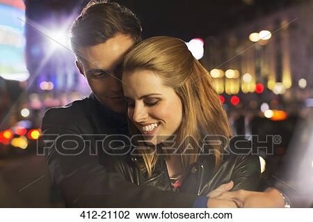 Stock Image - Couple hugging on city street at night . Fotosearch
