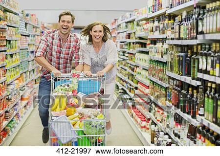 Couple playing with shopping cart in grocery store aisle View Large Photo Image Stock Photo - Couple playing with shopping cart in grocery store aisle. Fotosearch
