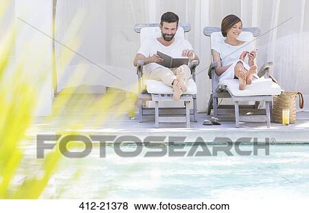 Stock Photo - Couple relaxing in lawn chairs by swimming pool. Fotosearch