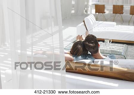 Couple relaxing together on sofa in modern living room View Large Photo Image Stock Image - Couple relaxing together on sofa in modern living room. Fotosearch