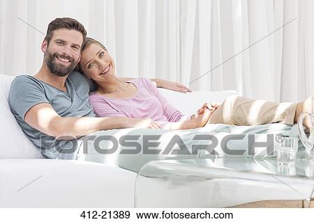 Couple relaxing together on sofa in modern living room View Large Photo Image Stock Photo - Couple relaxing together on sofa in modern living room. Fotosearch