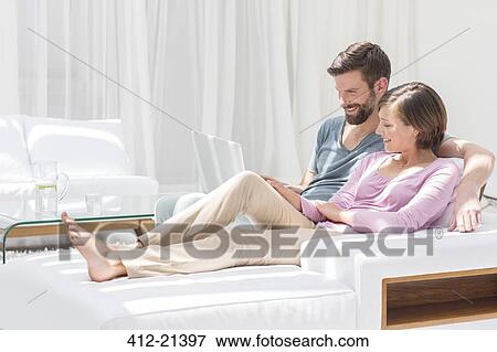 Couple using laptop on sofa in modern living room View Large Photo Image Stock Photo - Couple using laptop on sofa in modern living room. Fotosearch