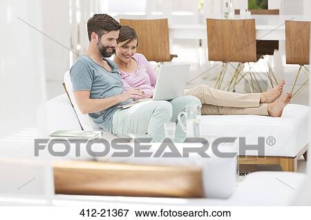 Couple using laptop together on daybed in modern living room View Large Photo Image Stock Photo - Couple using laptop together on daybed in modern living room. Fotosearch