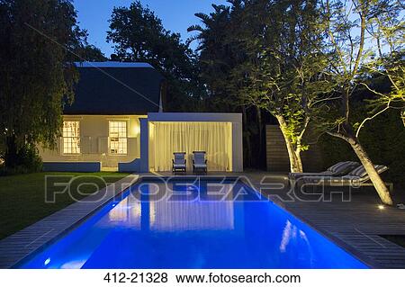 Lawn chairs on wooden deck by illuminated swimming pool at night View Large Photo Image Stock Photo - Lawn chairs on wooden deck by illuminated swimming pool at night. Fotosearch