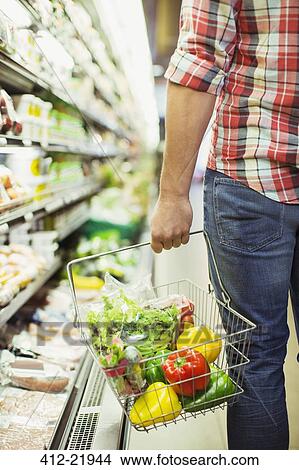 Picture - Man carrying full shopping basket in grocery store. Fotosearch