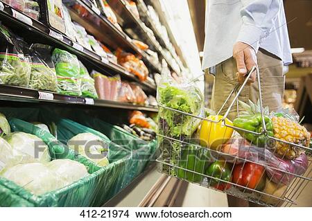 Picture - Man carrying full shopping basket in grocery store. Fotosearch