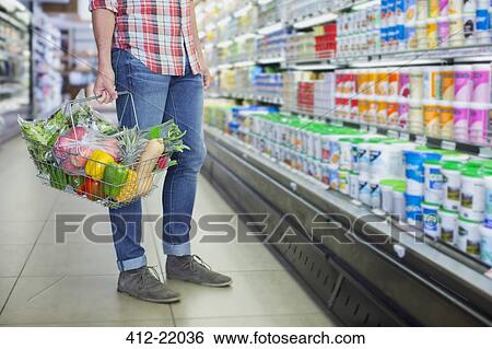 Man carrying full shopping basket in grocery store View Large Photo Image Stock Photograph - Man carrying full shopping basket in grocery store. Fotosearch