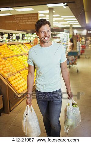 Man carrying shopping bags in grocery store View Large Photo Image Stock Photo - Man carrying shopping bags in grocery store. Fotosearch