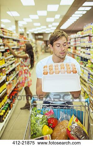 Stock Photography - Man examining carton of eggs in grocery store. Fotosearch