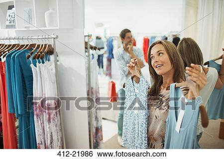 Stock Photograph - Man helping girlfriend pick dresses in clothing store. Fotosearch
