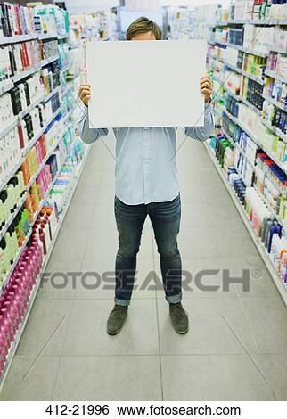 Stock Photograph - Man holding blank card in grocery store aisle. Fotosearch