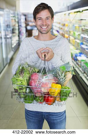 Stock Image - Man holding full shopping basket in grocery store. Fotosearch